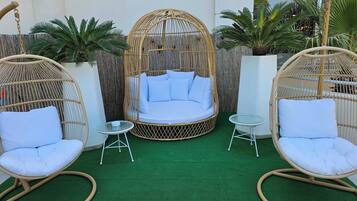 A cozy outdoor seating area with a wicker swing chair, a cushioned bench, and a small round table.