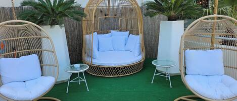 A cozy outdoor seating area with a wicker swing chair, a cushioned bench, and a small round table.