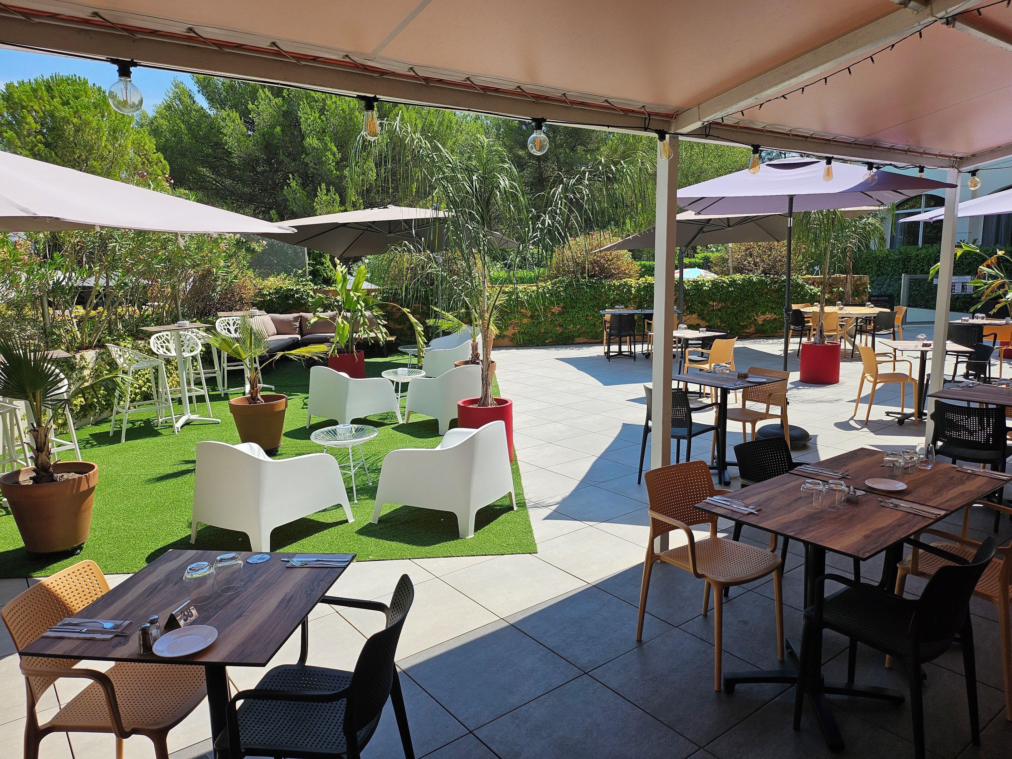 An outdoor patio area with tables and chairs, surrounded by potted plants and trees.