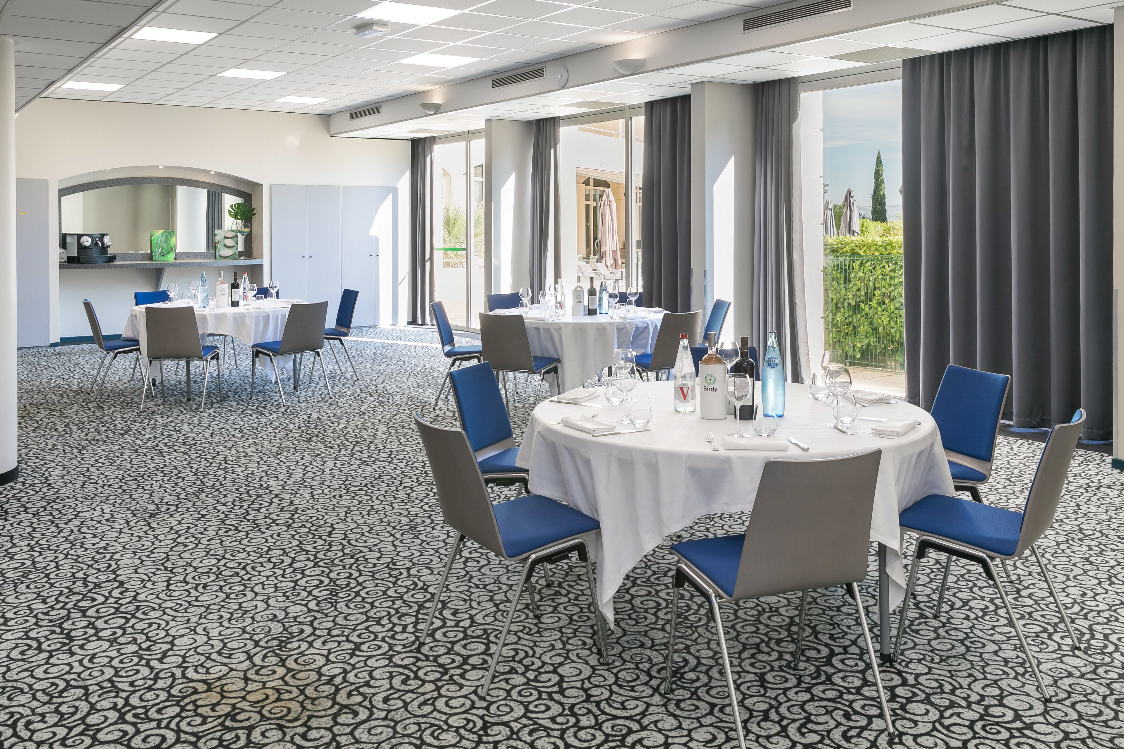 Ein Konferenzraum mit runden Tischen, blauen Stühlen und einem gemusterten Teppich.