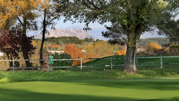 Un campo de golf con una cerca de madera, árboles con follaje otoñal y montañas al fondo.