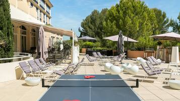 Ein Poolbereich mit Liegestühlen, Sonnenschirmen und einem Tischtennis-Tisch.