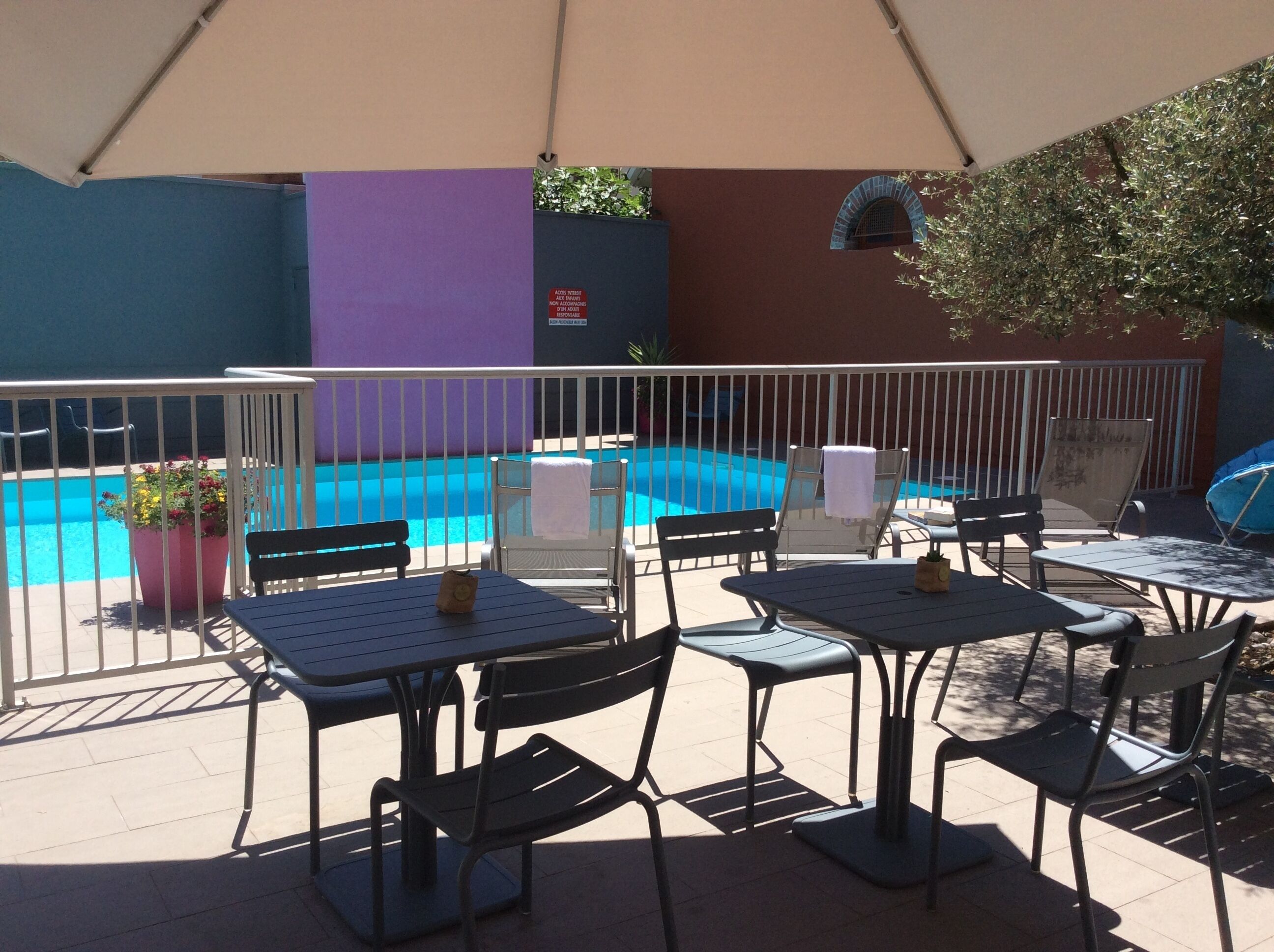 Un espace extérieur aménagé avec des tables et des chaises, une piscine et un bâtiment dont l’un des murs est peint en violet.