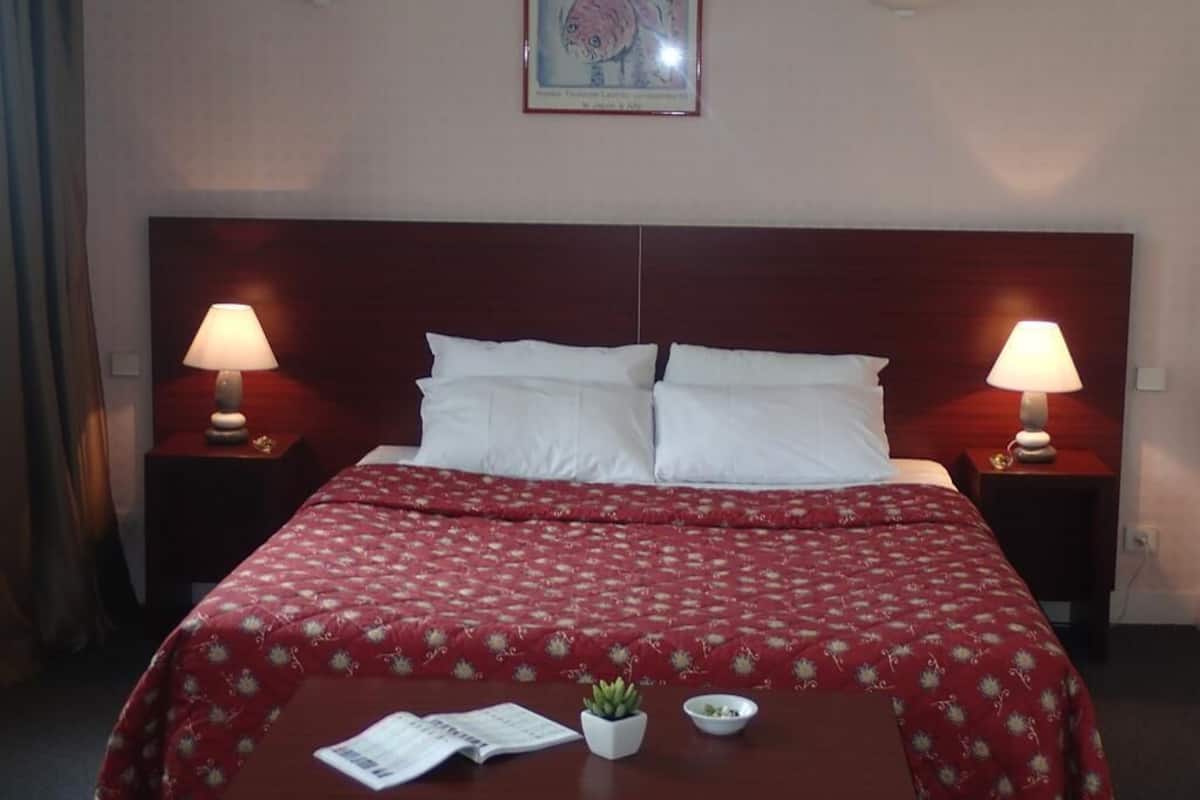 Habitación de hotel con cama doble, dos mesitas de noche con lámparas, una mesita pequeña con una planta y un cuenco, y un cuadro en la pared.