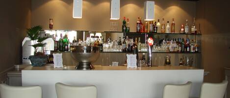 A bar area with a counter, multiple shelves of bottles, and four chairs.