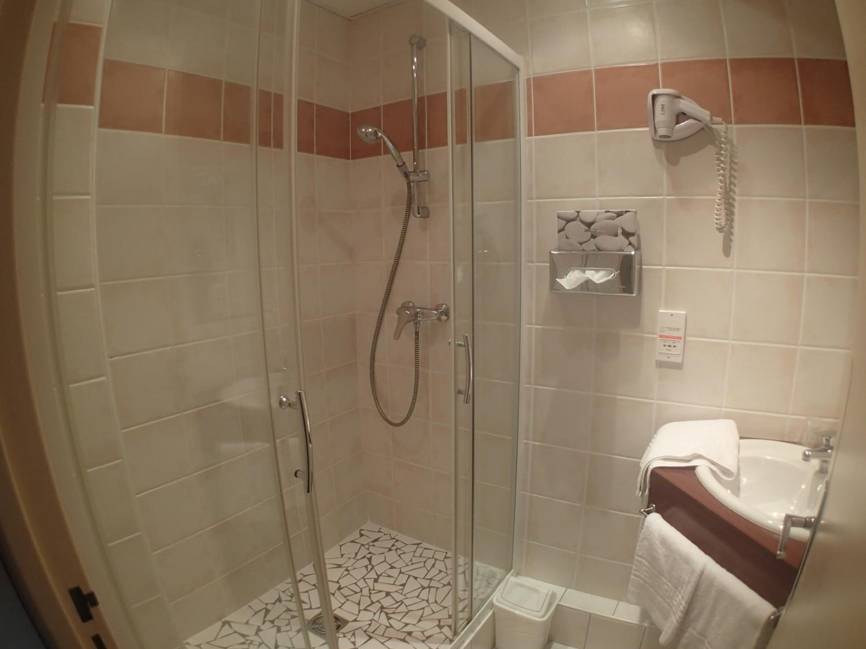 Une douche fermée par des parois en verre, dotée d’un pommeau de douche à main, d’un porte-serviettes et d’un distributeur de savon.