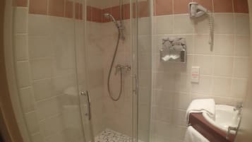 Une douche fermée par des parois en verre, dotée d’un pommeau de douche à main, d’un porte-serviettes et d’un distributeur de savon.