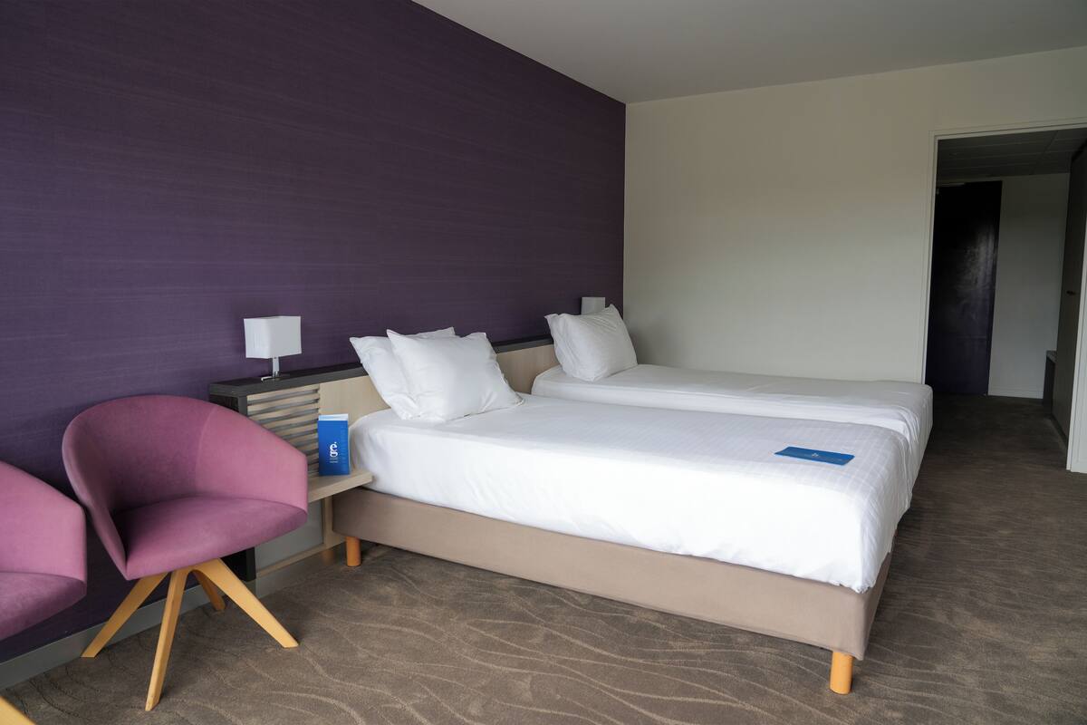 A hotel room with a bed, a desk, a chair, and a purple wall.