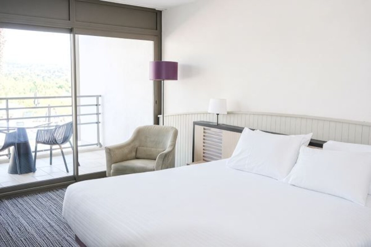 Habitación de hotel con una cama grande, una silla, una mesa y un balcón con vistas.