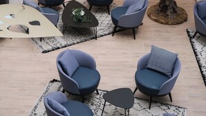 Un área de estar moderna con varias opciones de asiento, un árbol decorativo y un mural abstracto y colorido.