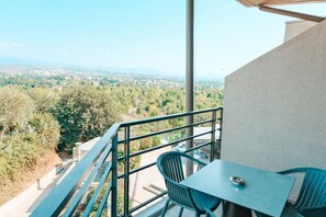 Un balcón con mesa y sillas, con vista a un paisaje urbano con árboles y edificios.