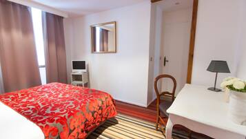 A hotel room with a bed, a desk, a chair, a mirror, and a door.