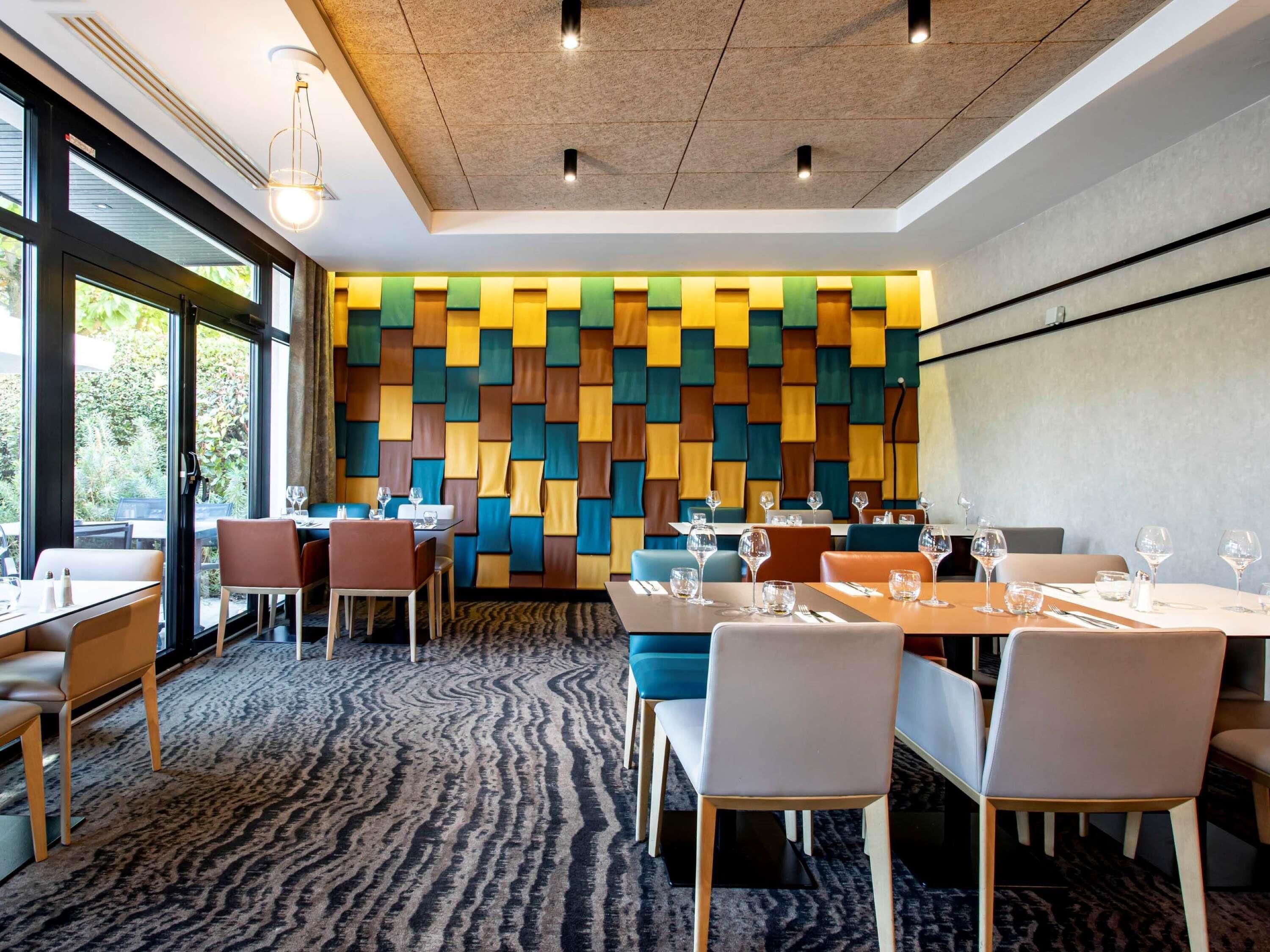 A modern restaurant interior with a patterned wall, tables with chairs, and a carpeted floor.