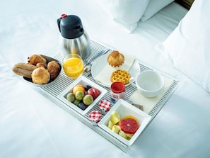 A breakfast tray with croissants, waffles, fruit, and juice on a bed.