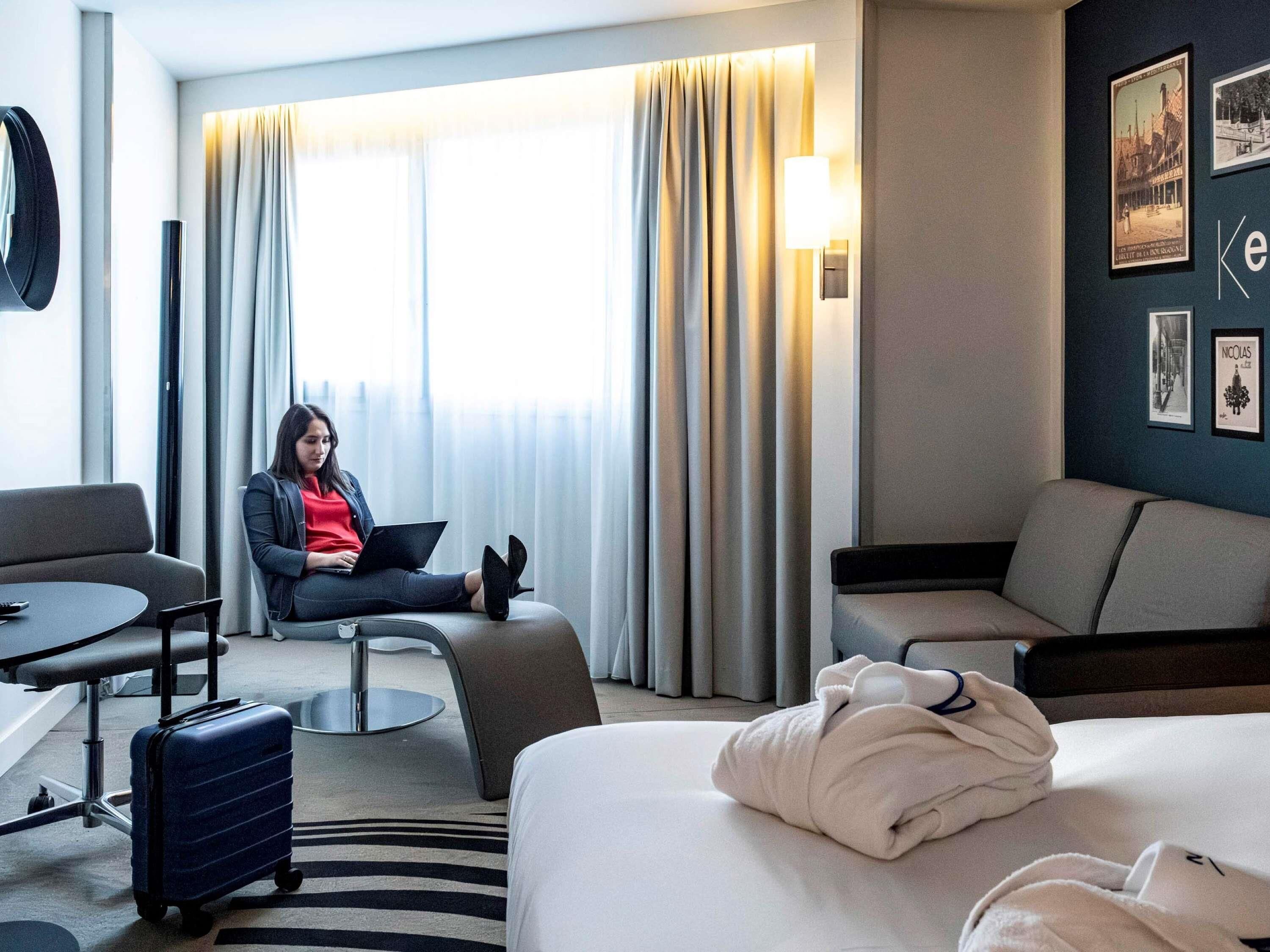 Una habitación de hotel moderna con cama, escritorio, silla y ventana con cortinas.