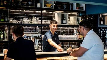 Zona de bar con estantes llenos de botellas y vasos, barra y una persona sirviendo bebidas.