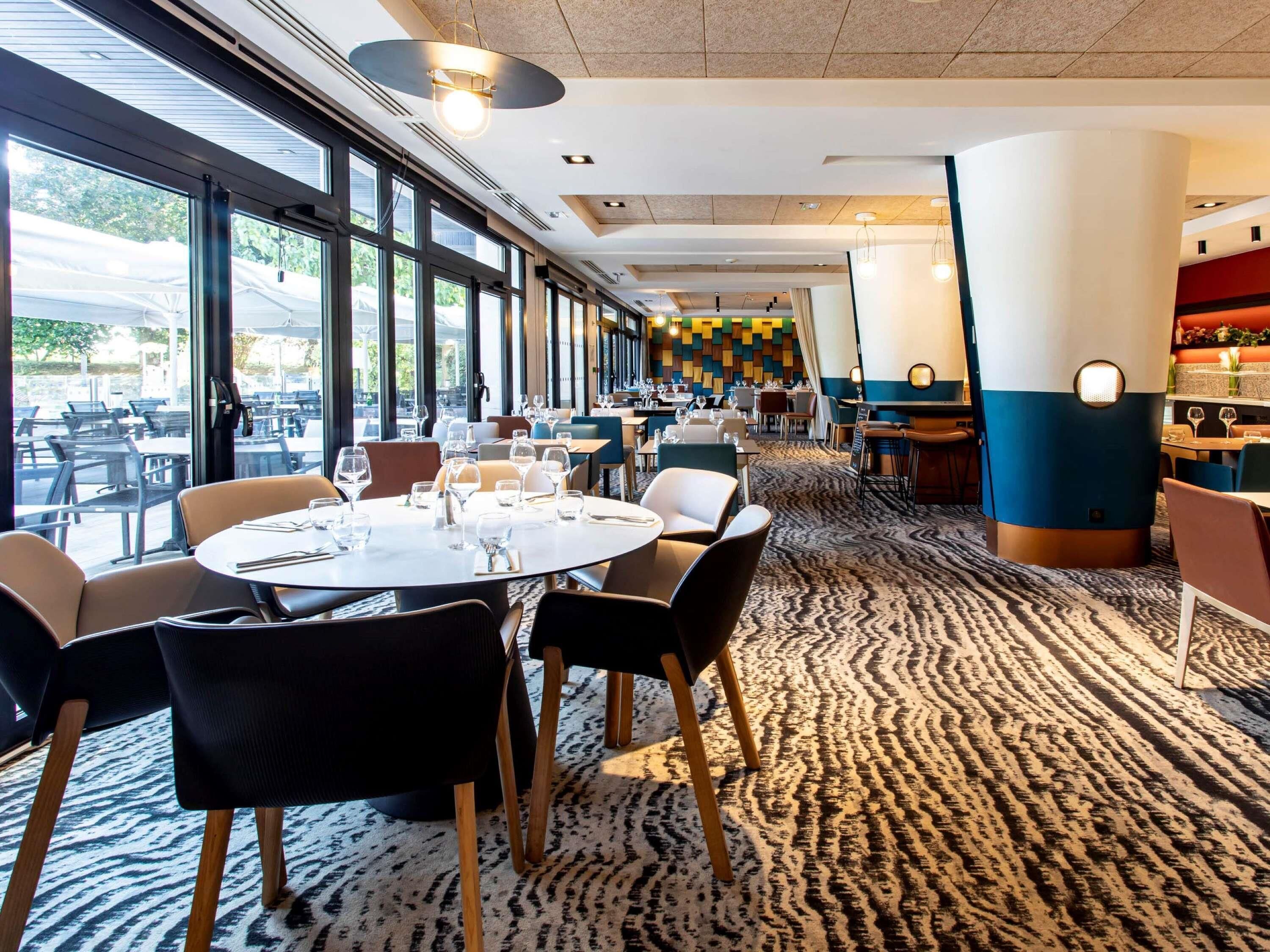 Ein modernes Restaurant mit runden Tischen, Stühlen und einem gemusterten Teppich.