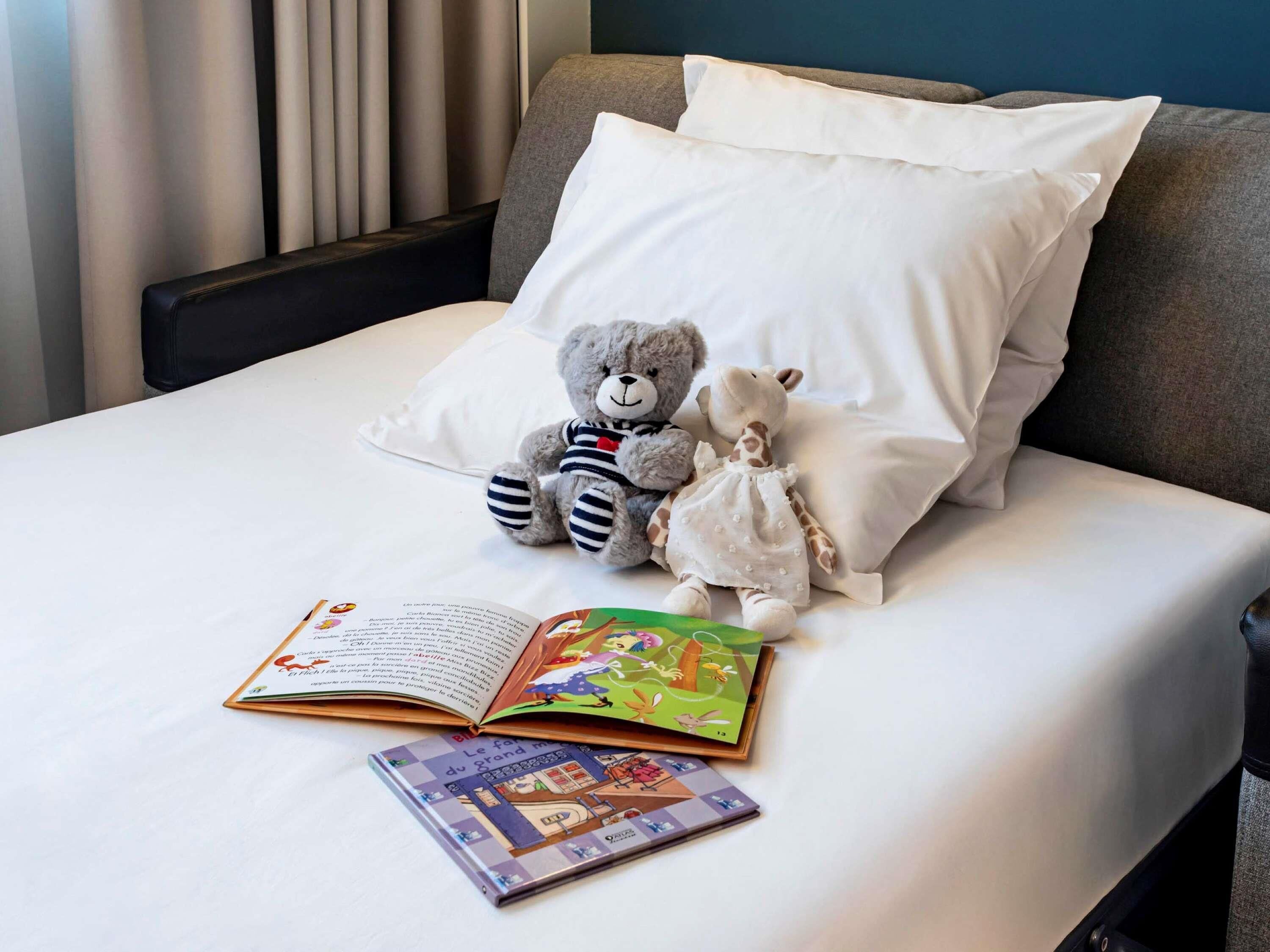 A bed with a white pillow, two stuffed animals, and an open book.