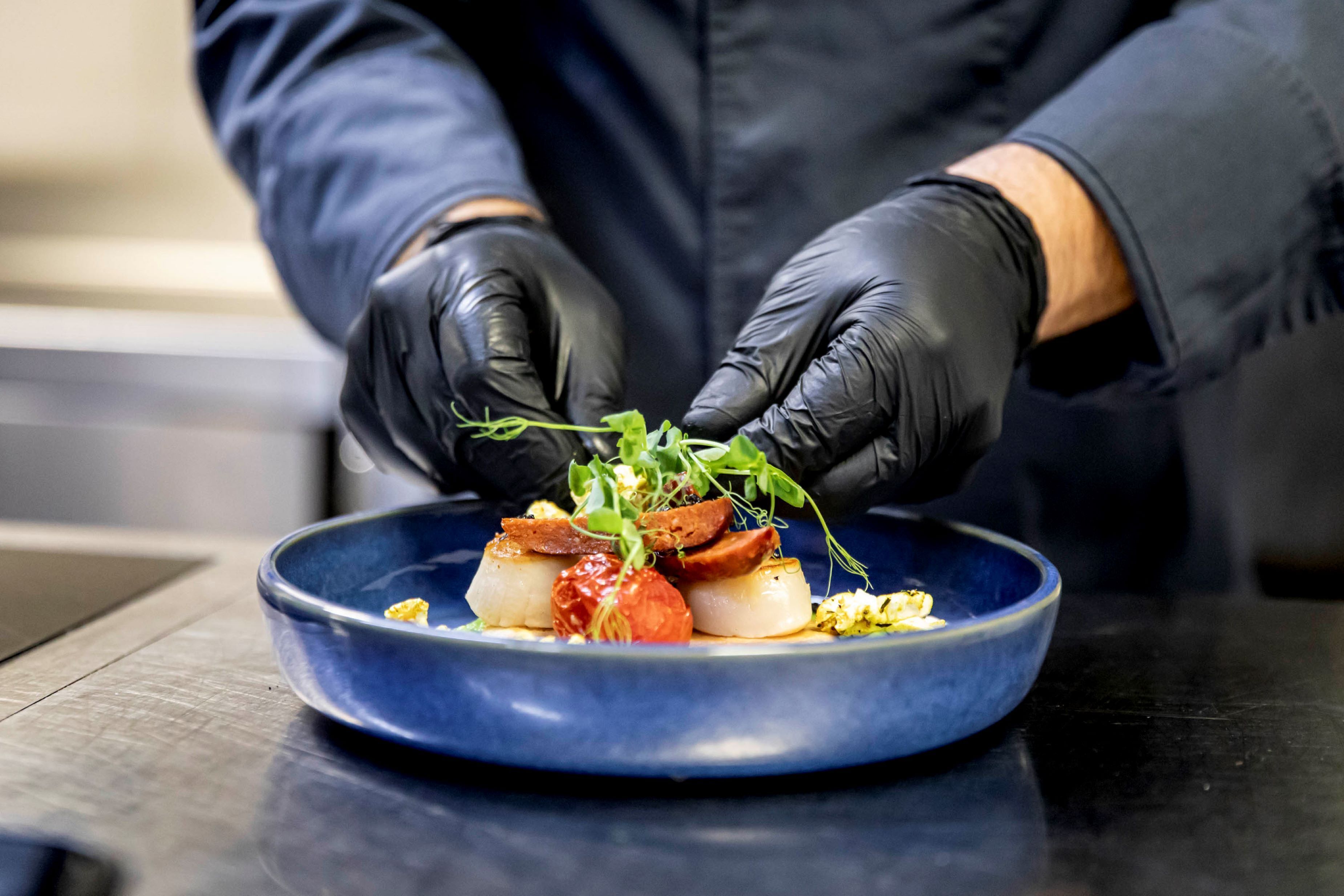 A person in black gloves placing food on a blue plate.
