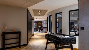 Un moderno hall de hotel con mesa de fútbol, suelo de madera y vista al comedor.