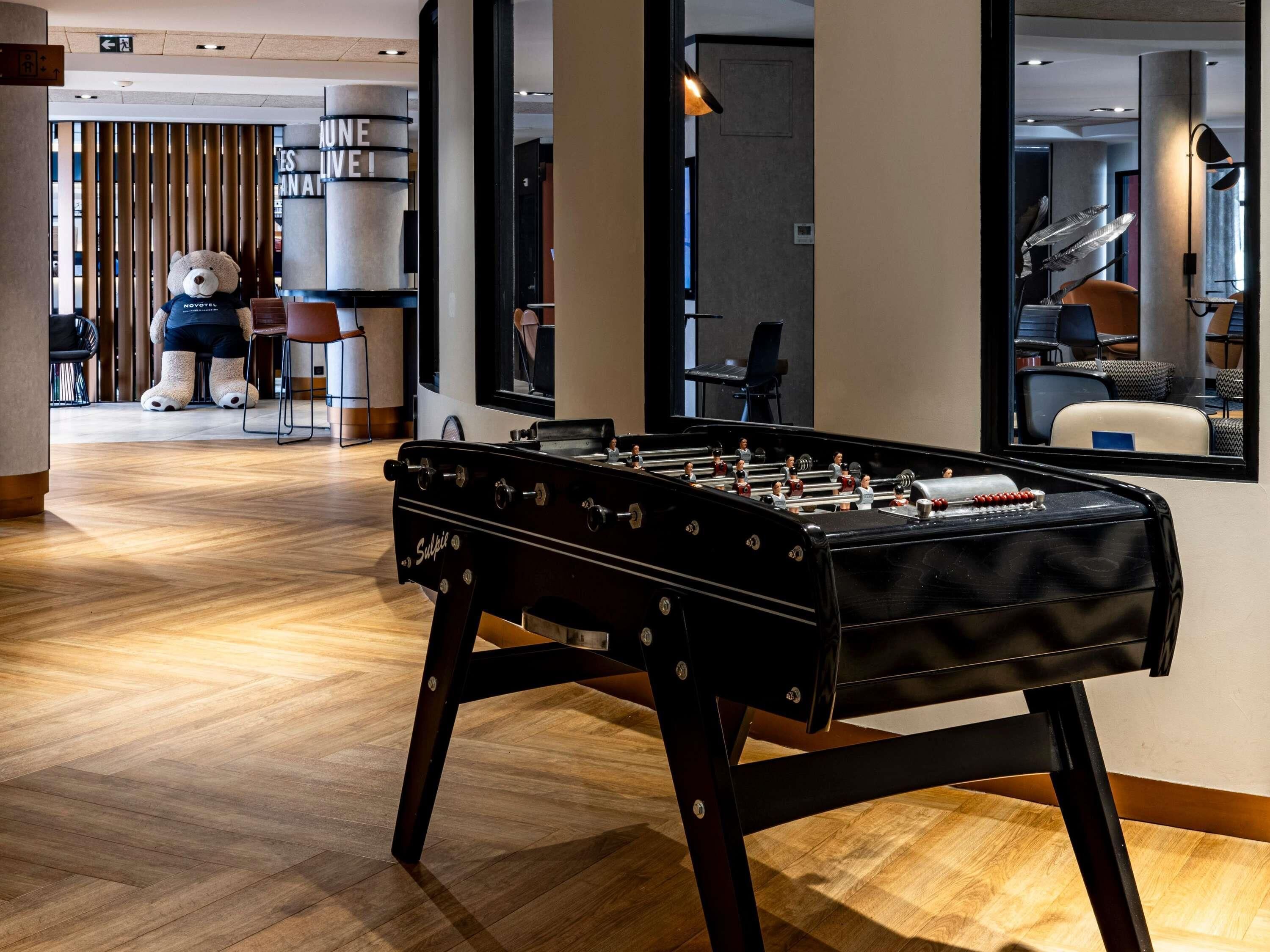 Un moderno vestíbulo de hotel con una mesa de fútbol de mesa, suelo de madera y un amplio ventanal.
