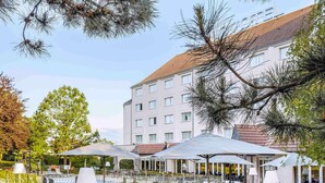 Un patio de hotel con mobiliario exterior, una piscina y un edificio al fondo.