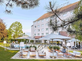 Un patio de hotel con mobiliario exterior, una piscina y un edificio al fondo.