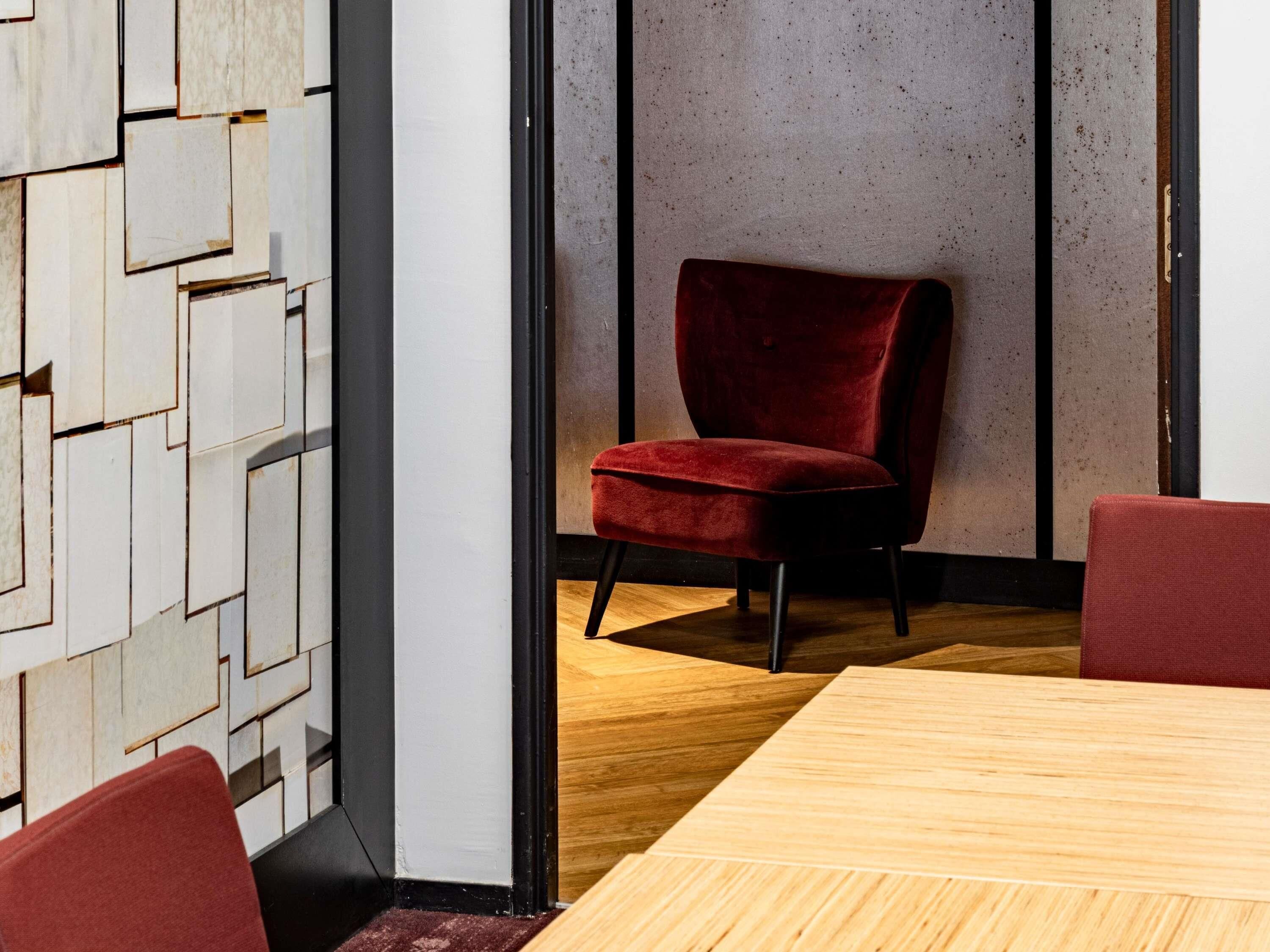 Un salón de conferencias con una mesa de madera, sillas rojas y un muro con diseño geométrico.