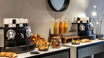 A breakfast buffet with coffee machines, croissants, fruit, and juice.