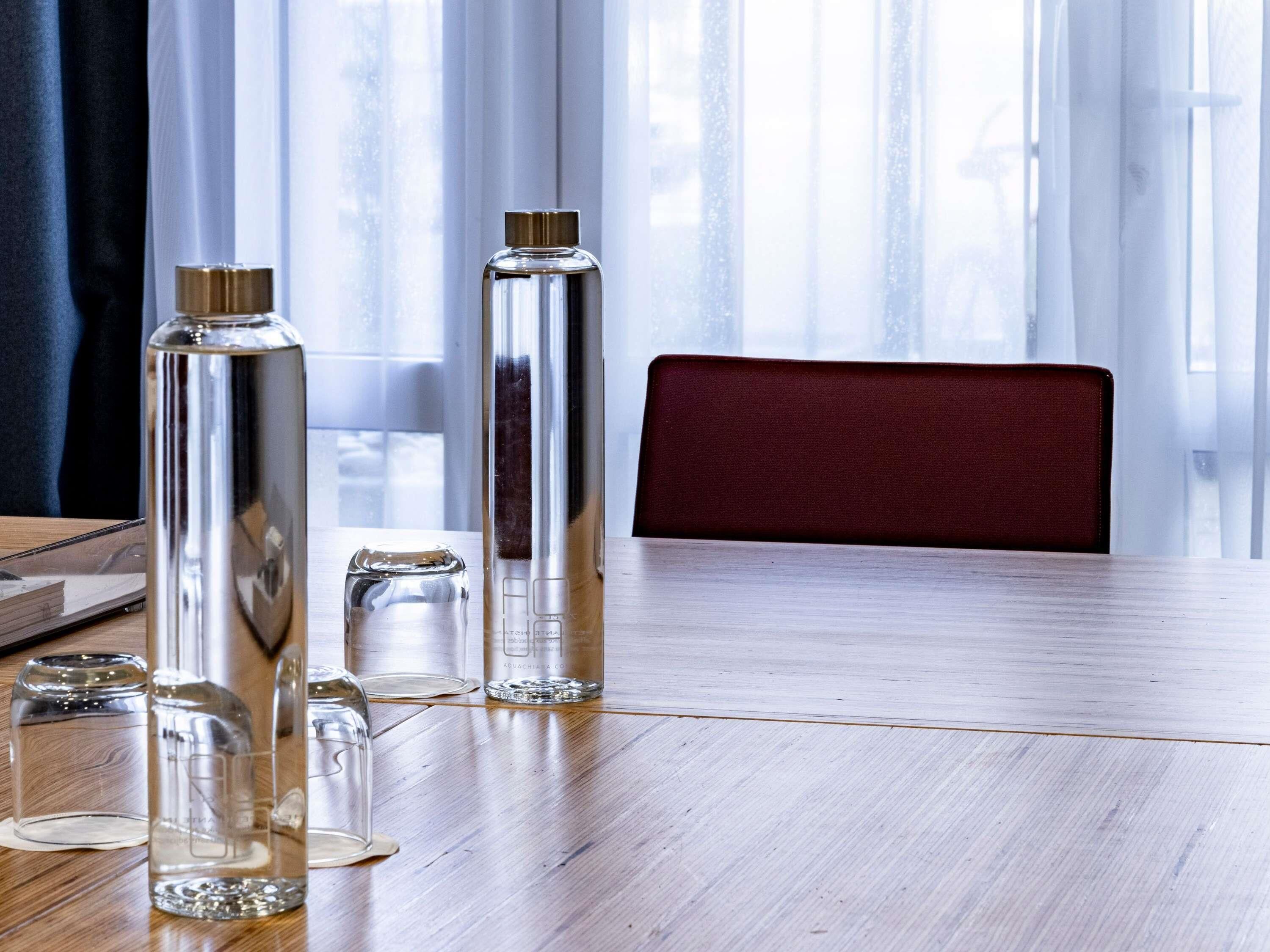 A wooden table with clear glass bottles and a metal container, a red chair, and a window with curtains.