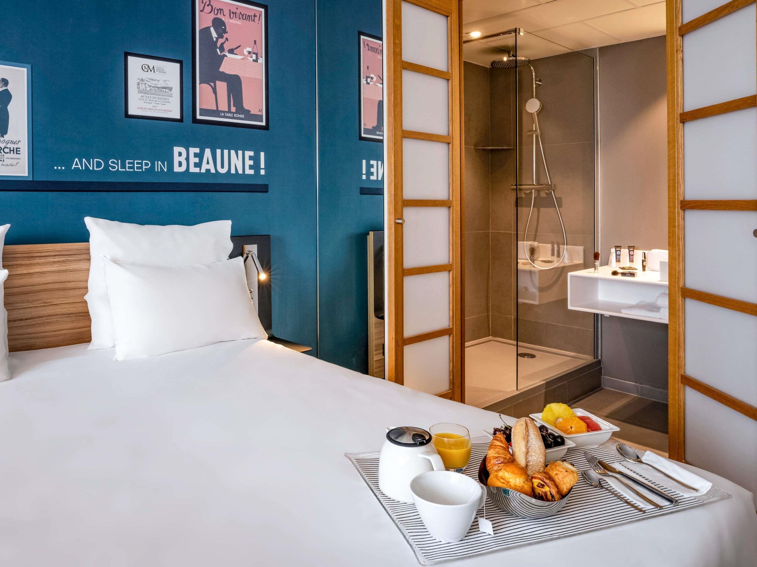 A hotel room with a bed, a breakfast tray, a shower, and a wall with posters.