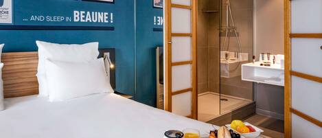 A hotel room with a bed, a breakfast tray, a shower, and a wall with posters.