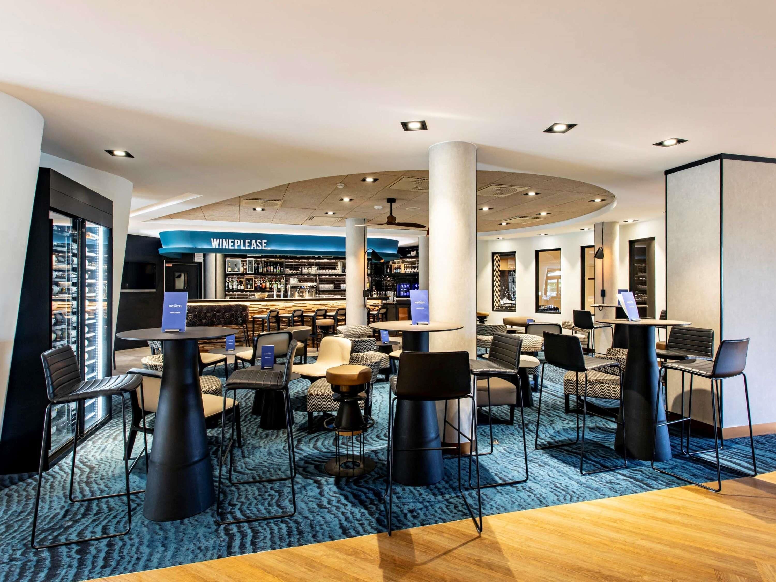 A modern hotel lobby with a bar area, seating arrangements, and a visible wine section.