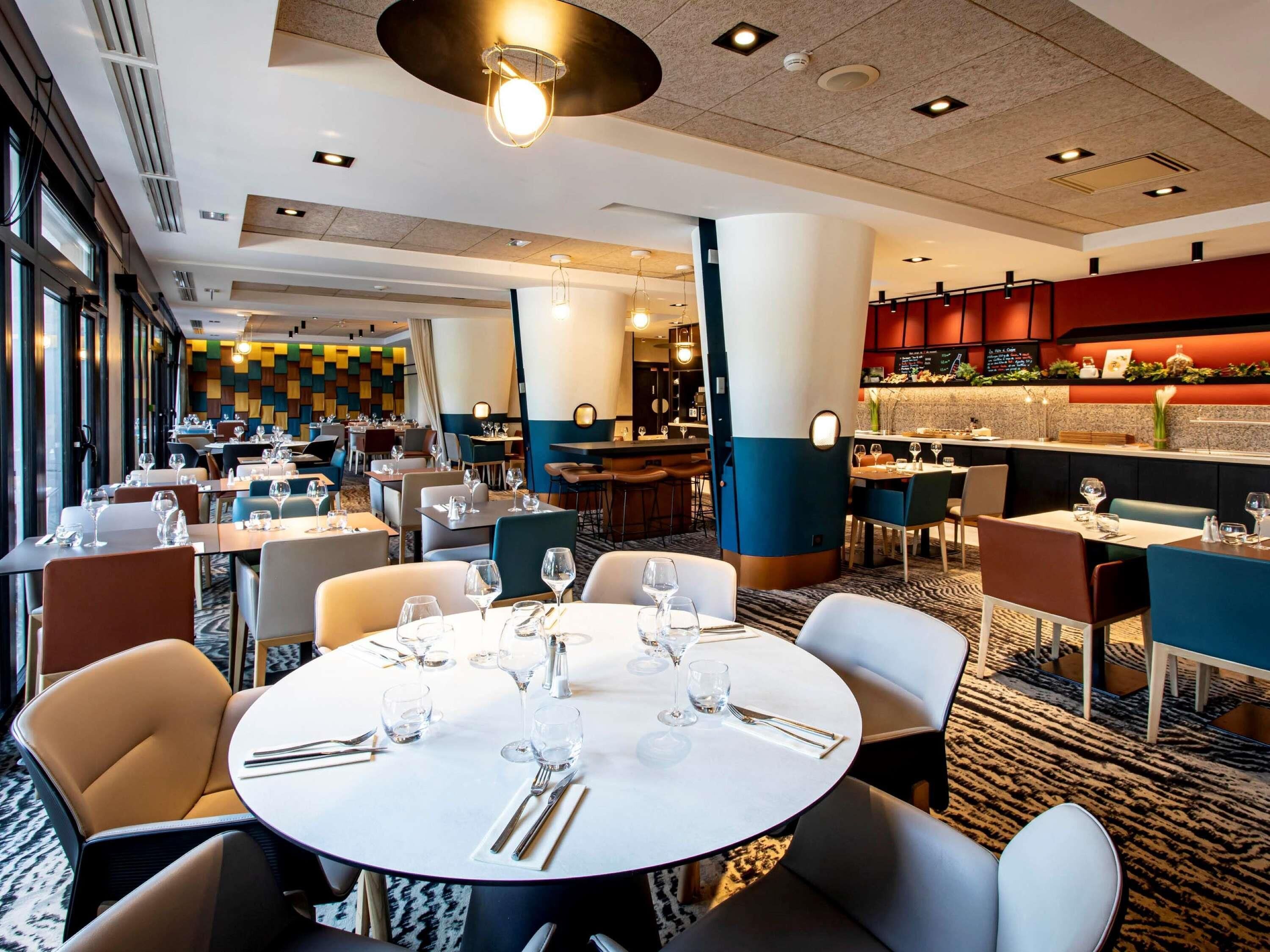 Un espace de restauration d’hôtel avec des tables rondes, des chaises et un bar.