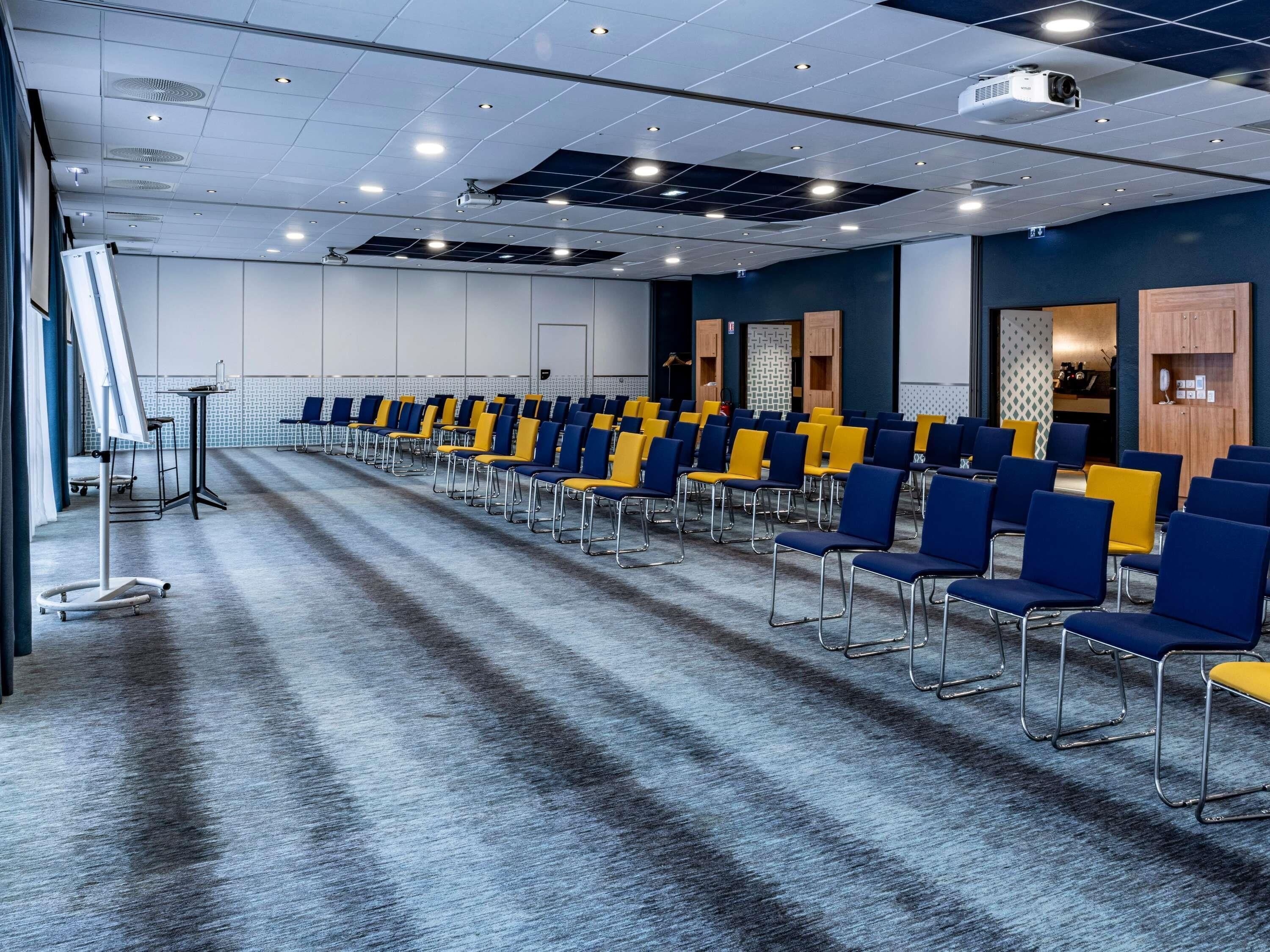 A conference room with rows of chairs, a projector, and a carpeted floor.