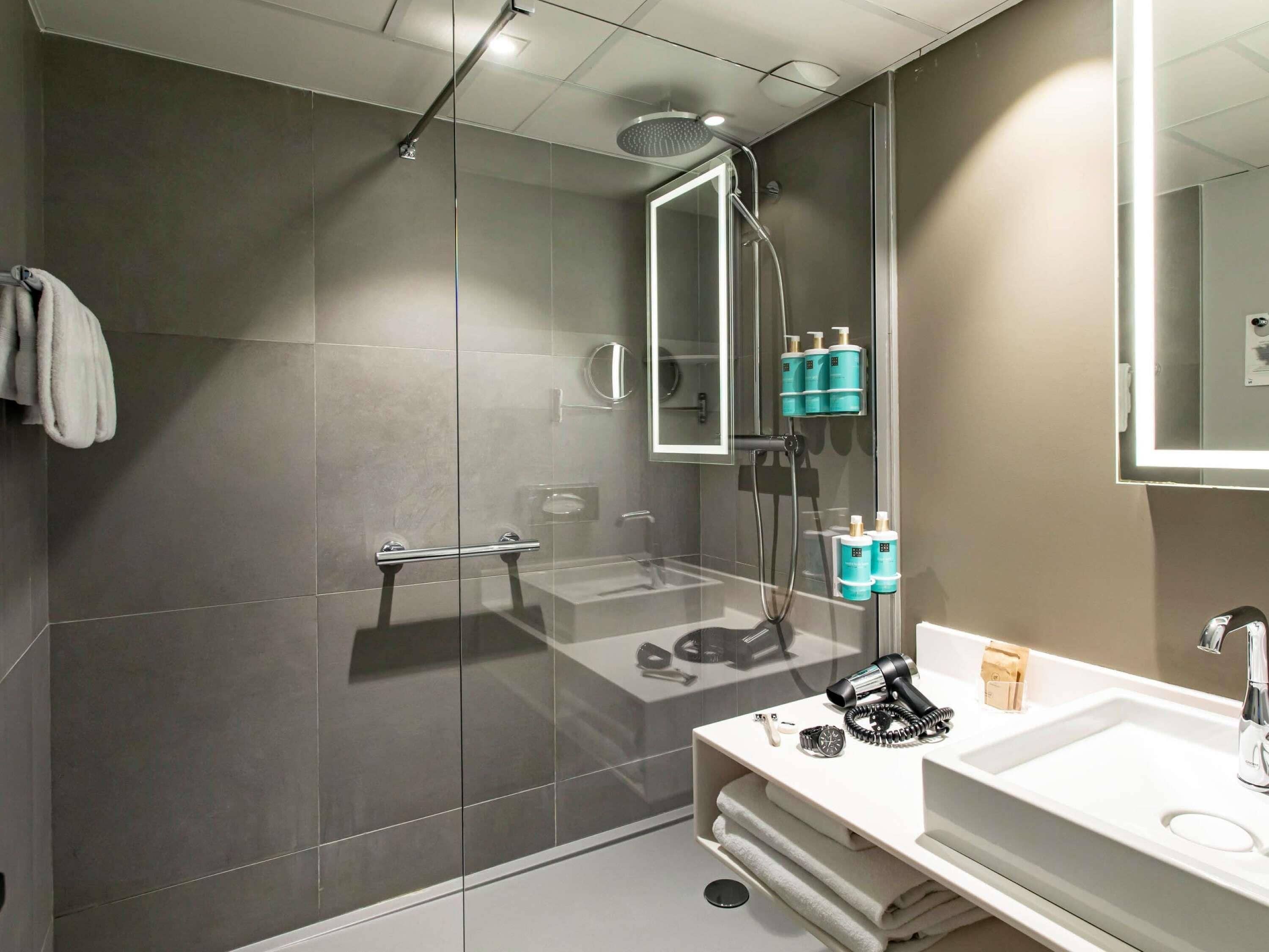 Une salle de bain moderne avec une douche à parois de verre, un grand miroir et un lavabo blanc doté d’un robinet chromé.