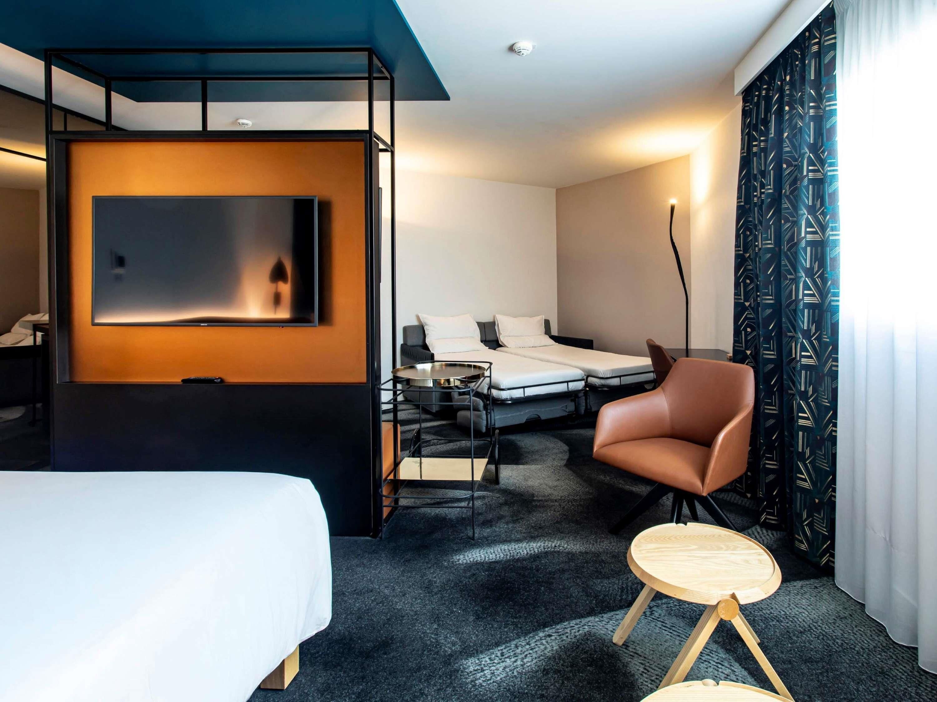 A modern hotel room with a bed, a sofa, a desk, and a small table.
