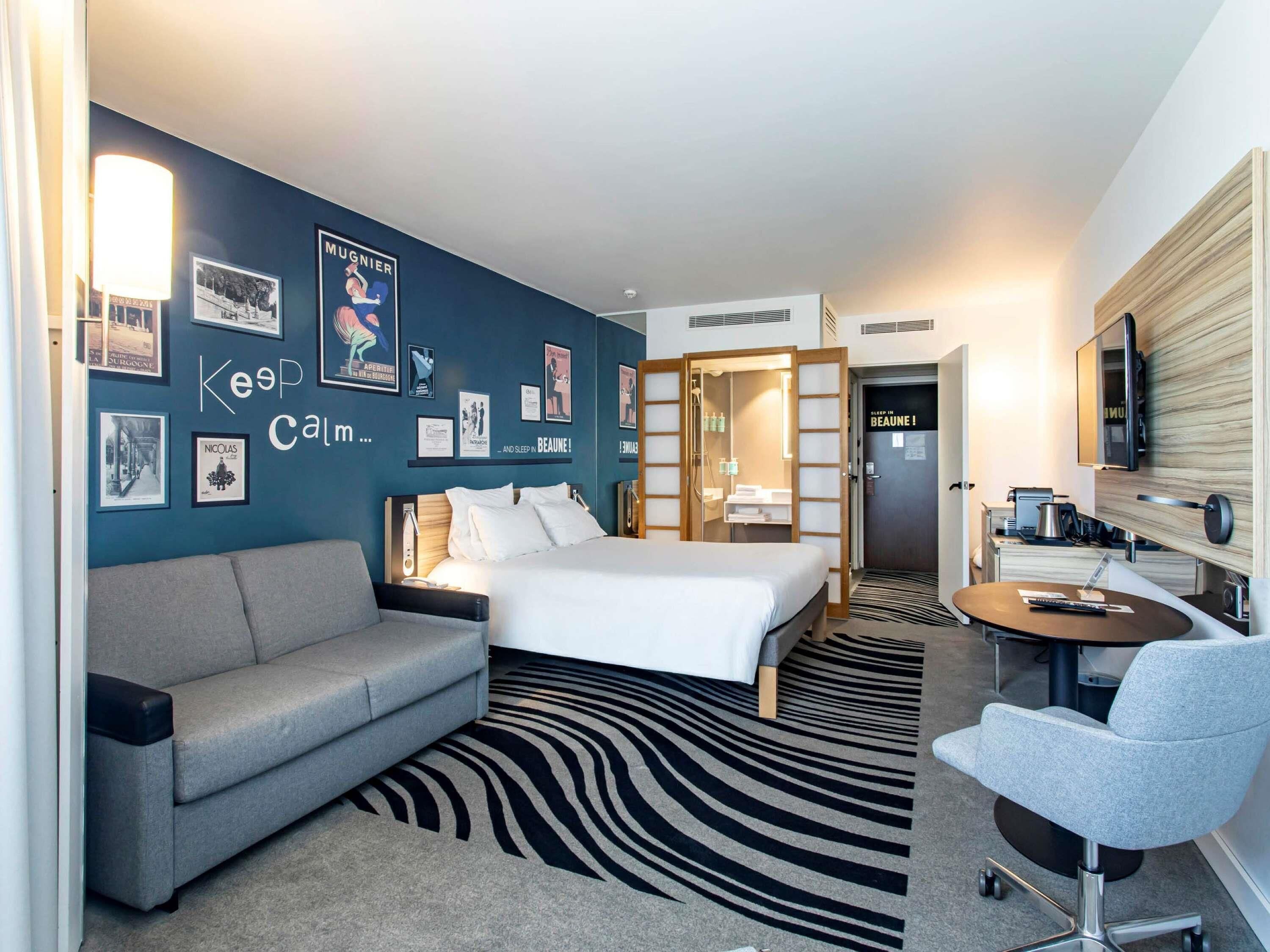 A hotel room with a bed, a sofa, a desk, and a TV.