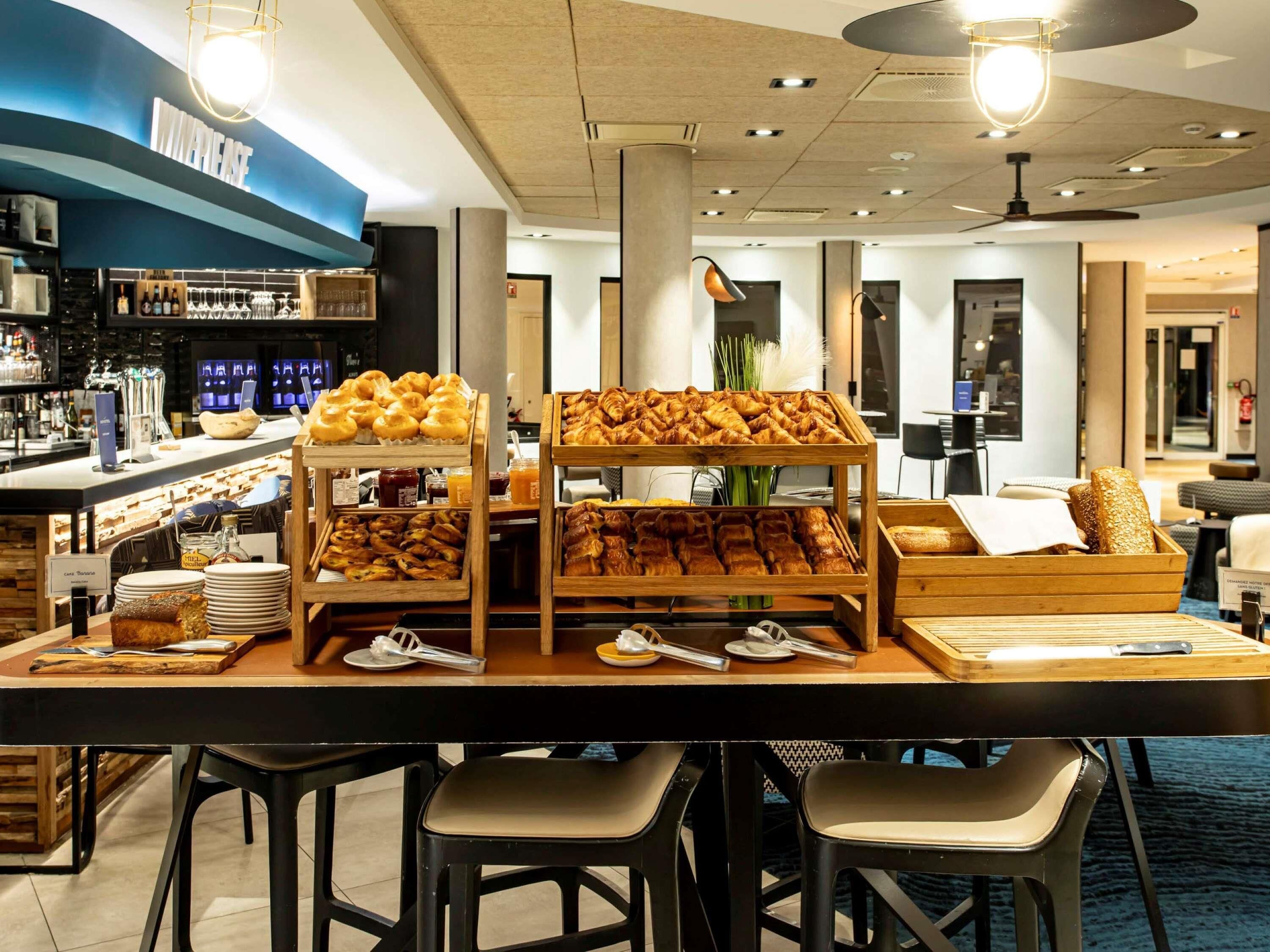 A breakfast bar with pastries and bread, bar stools, and a bar area with bottles.