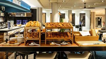 A breakfast bar with pastries and bread, bar stools, and a bar area with bottles.