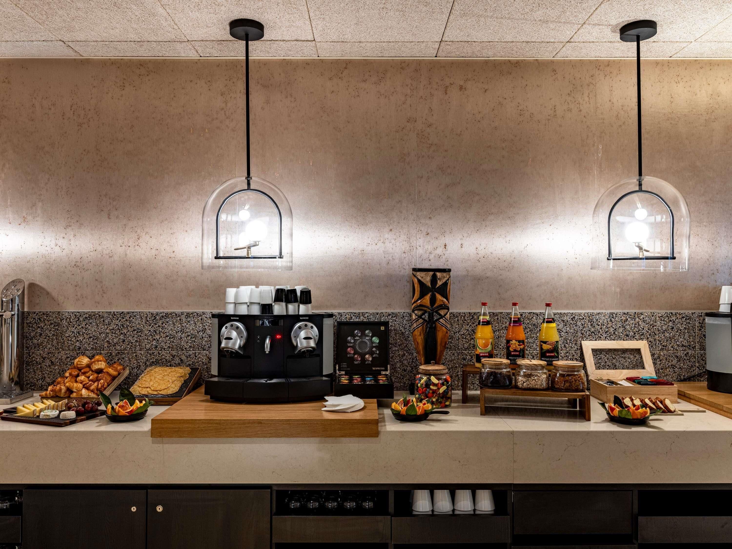 A modern kitchen with a coffee machine, a fruit display, and a variety of food items.