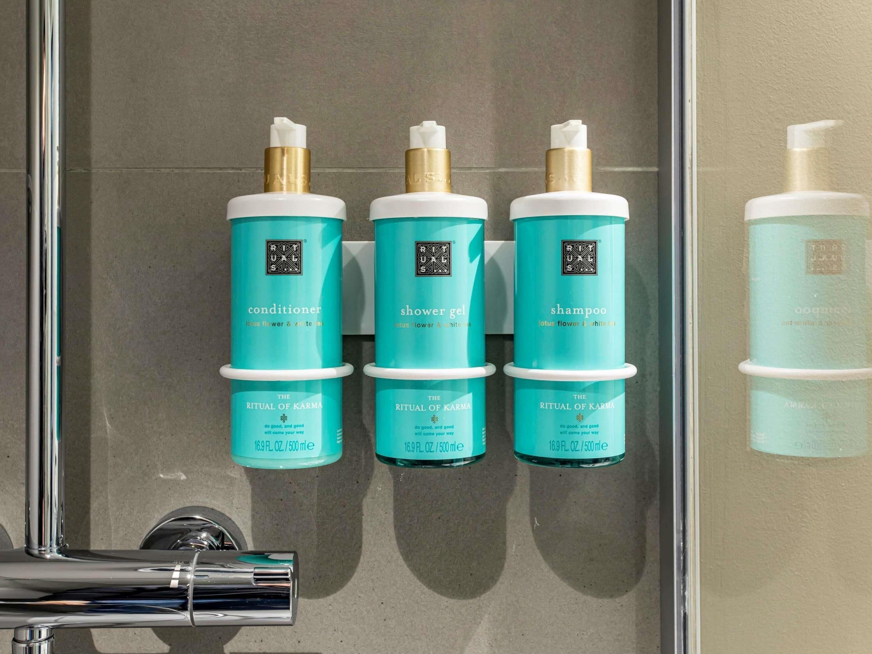 Three bottles of The Ritual of Karma conditioner, shower gel, and shampoo in a bathroom.