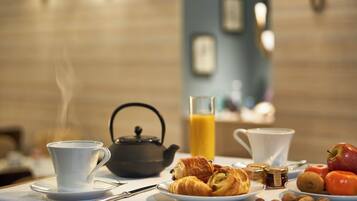 Una mesa con desayuno: tetera, cruasanes, manzanas, nueces y un vaso de jugo de naranja.