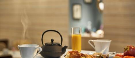 A breakfast setting with a teapot, croissants, apples, nuts, and a glass of orange juice on a table.