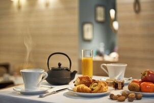 A breakfast setting with a teapot, croissants, apples, nuts, and a glass of orange juice on a table.