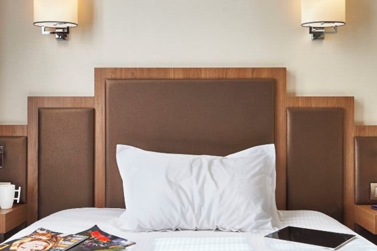 A hotel room with a large bed, two bedside tables, a nightstand, a magazine, and a tablet.