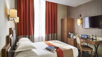 A hotel room with a bed, a desk with a laptop, a television, and a wardrobe.
