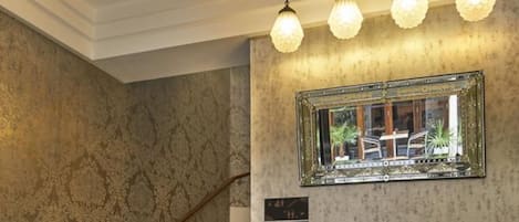 A lobby with a checkered floor, a large potted plant, a staircase, and a mirror on the wall.