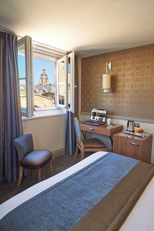 A hotel room with a bed, a desk with a laptop, a chair, a small table with a coffee pot and fruit, and a window with curtains. - Best Western Premier Hotel Bayonne Etche Ona - Bordeaux (Bordeaux)