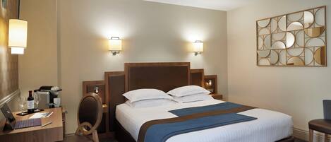 A hotel room with a bed, a desk, a chair, a lamp, and a wall art piece.